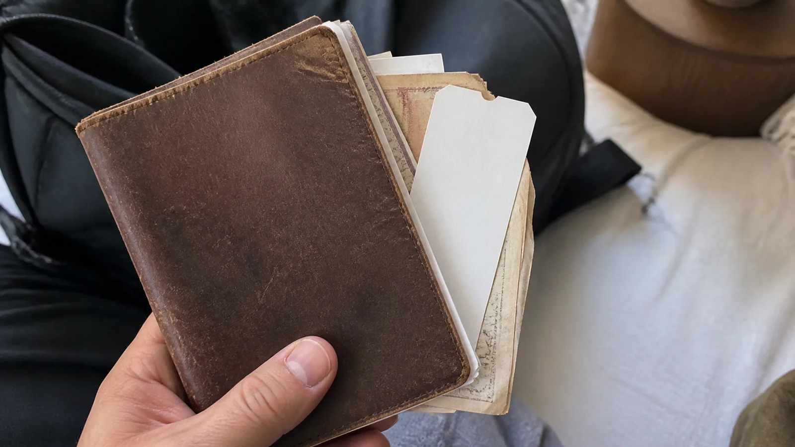 Hand holding a worn brown travel journal with papers tucked inside