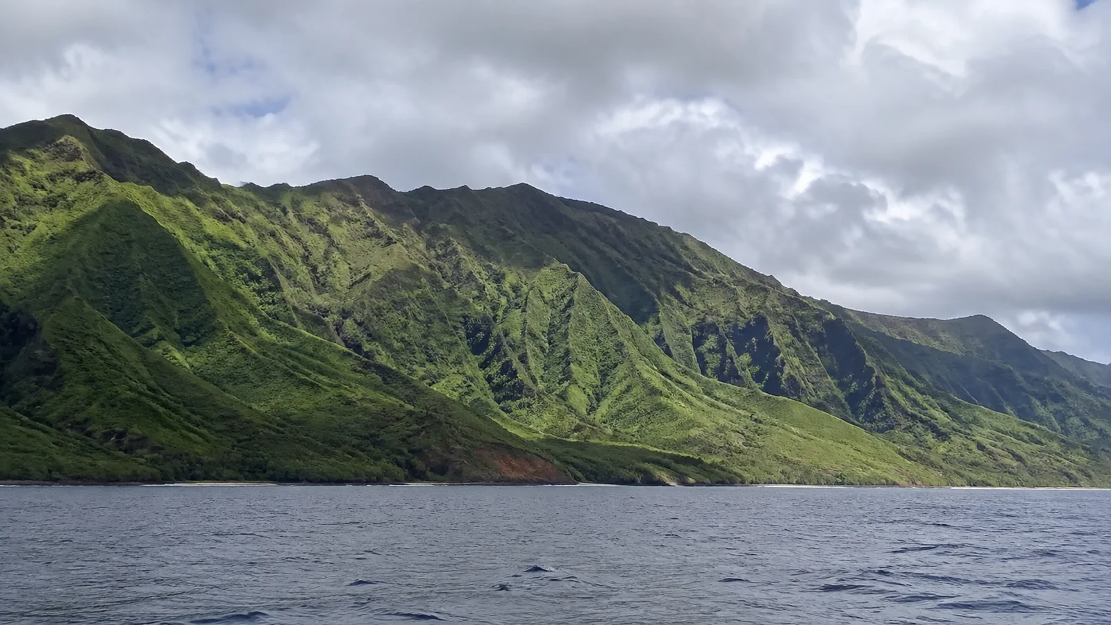 Steep green coastal ridges rising directly above blue ocean water.