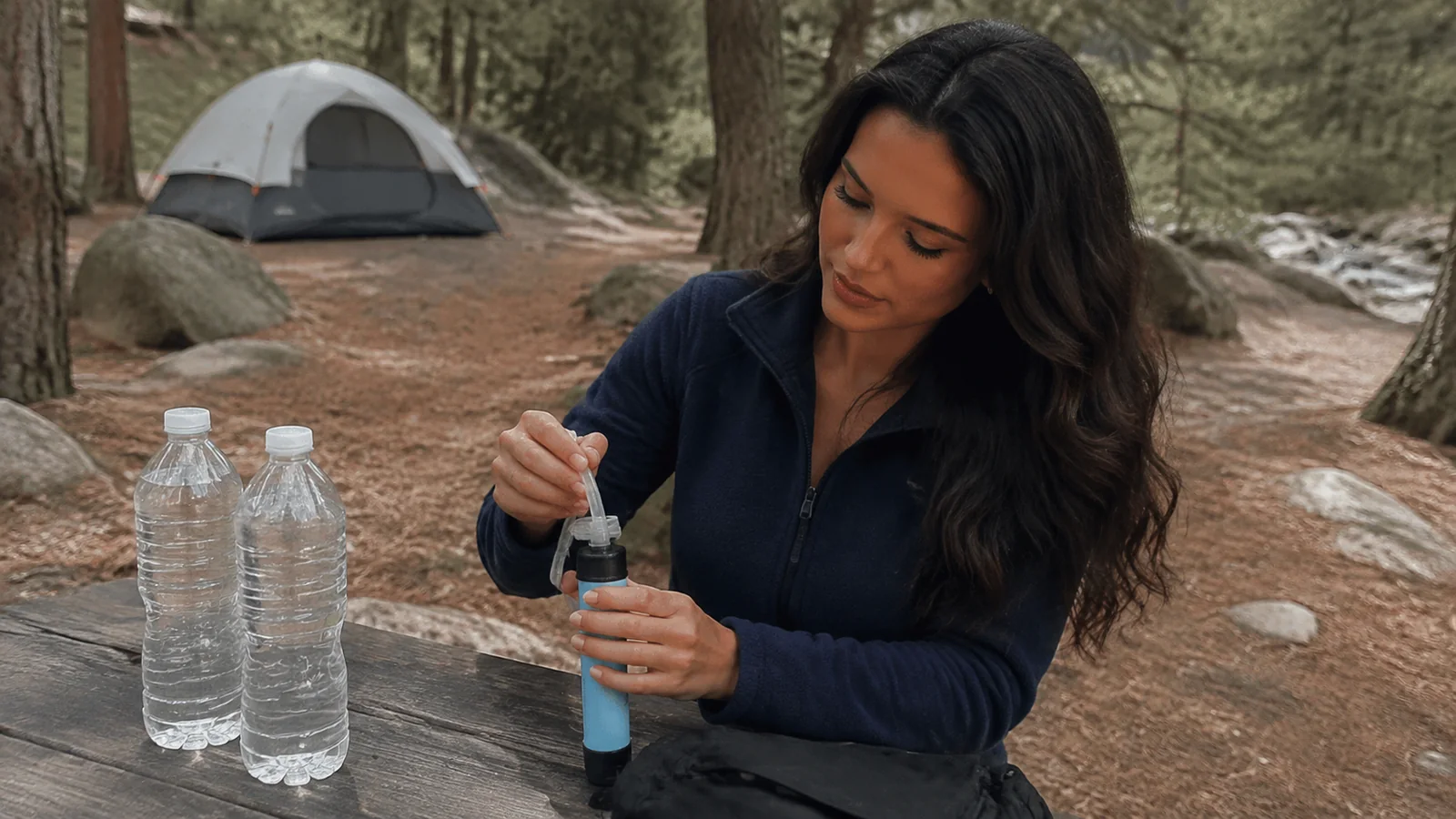 Woman preparing a small container beside water bottles at a campsite.