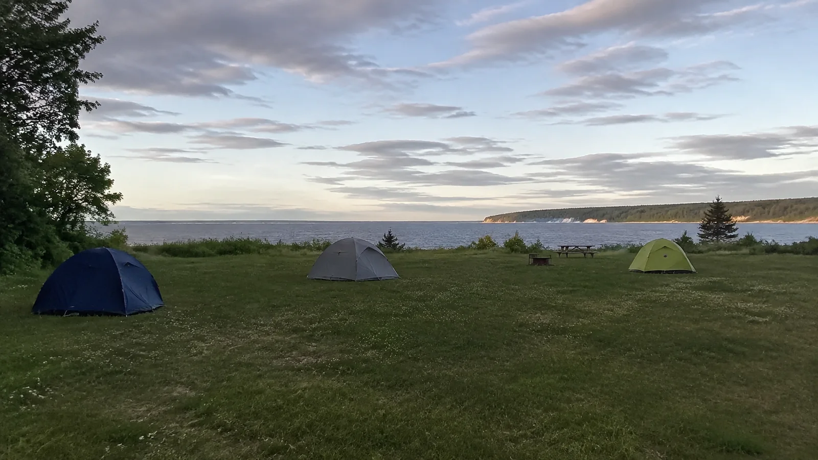 Small tents pitched on a grassy waterfront campground at dusk.