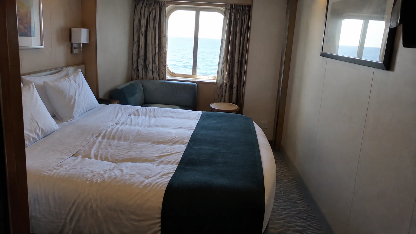 Cruise cabin with a double bed and blue sofa beside an ocean-view window