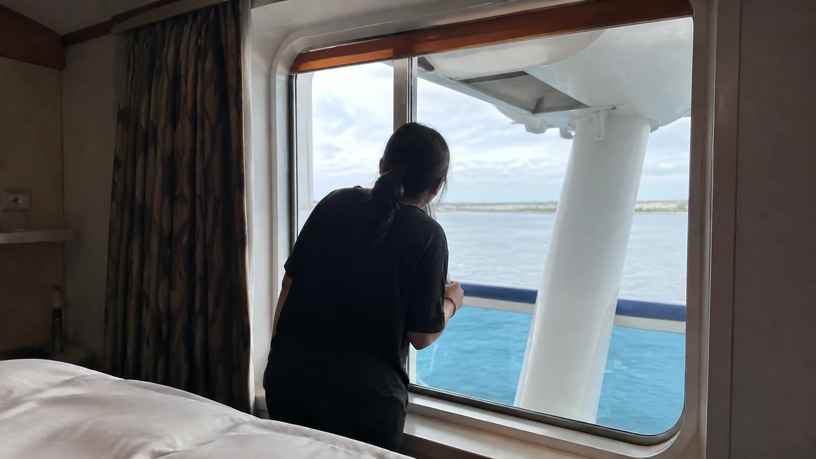 Woman looking through a cruise cabin window past a white support toward the sea