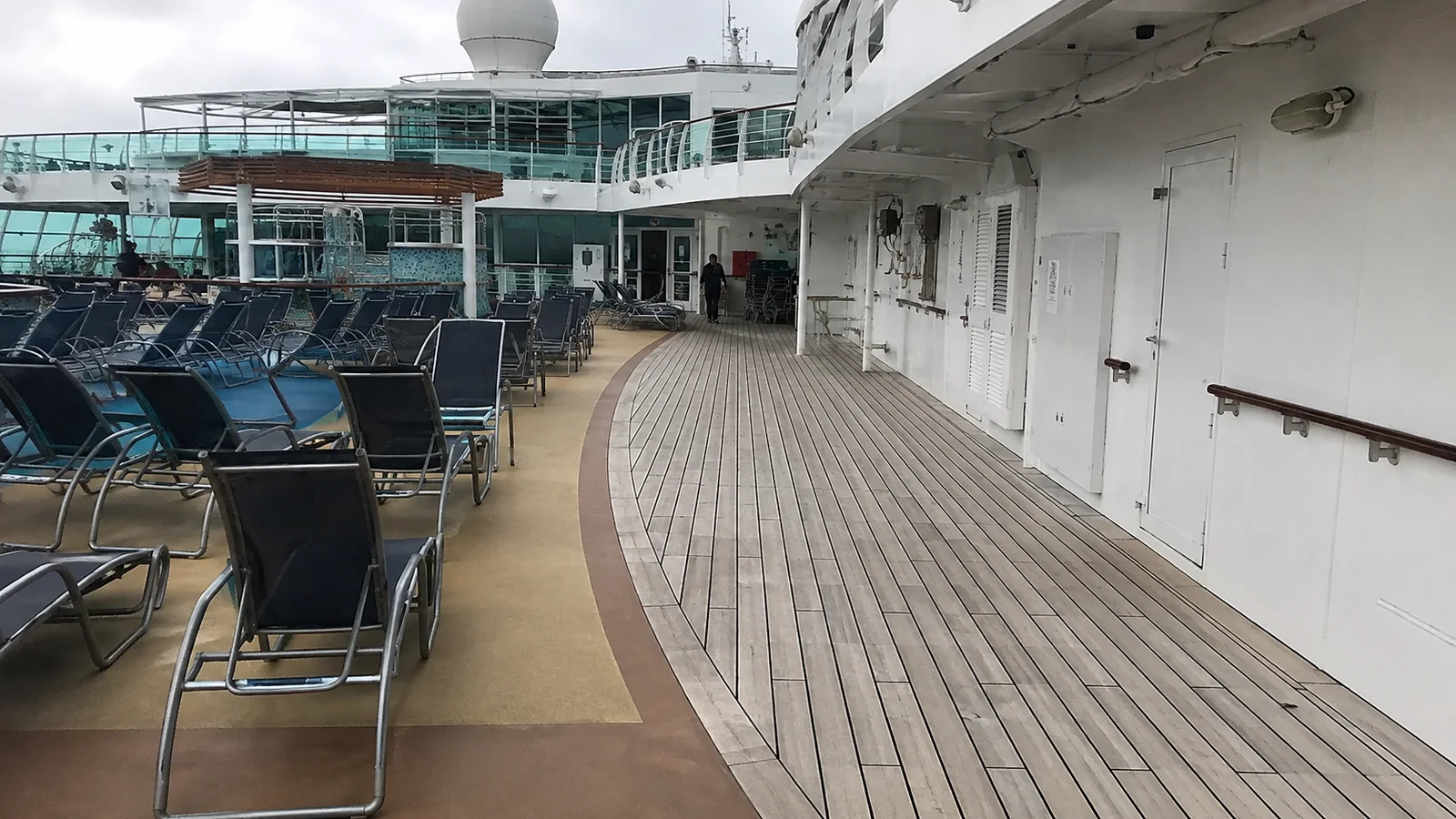 Curving wooden cruise ship walkway beside rows of lounge chairs