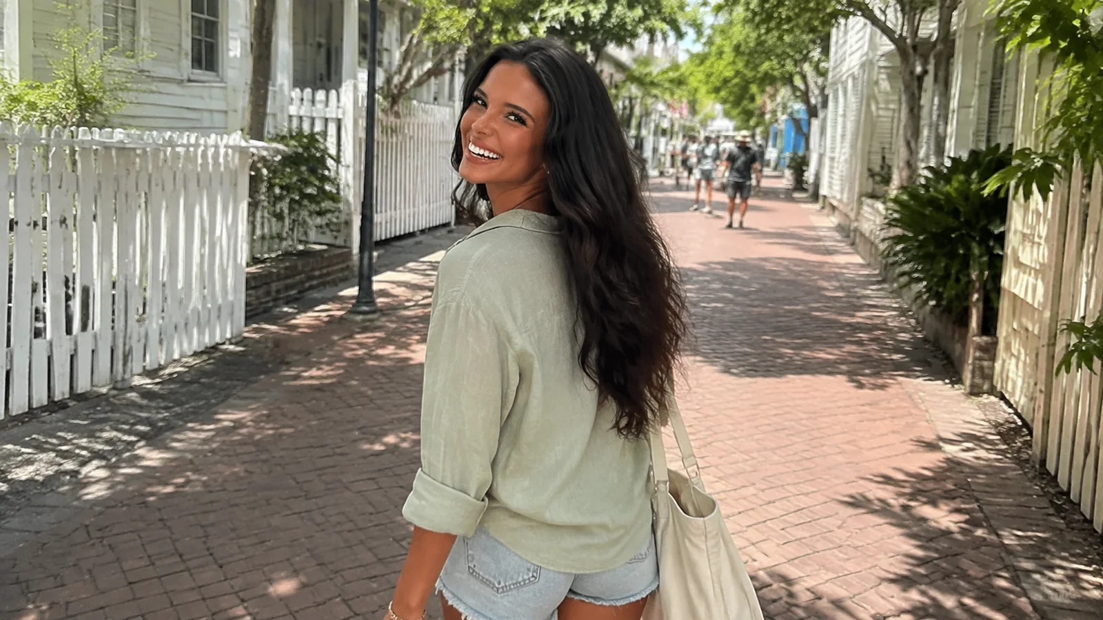 Smiling woman walking along a shaded brick sidewalk beside white picket fences