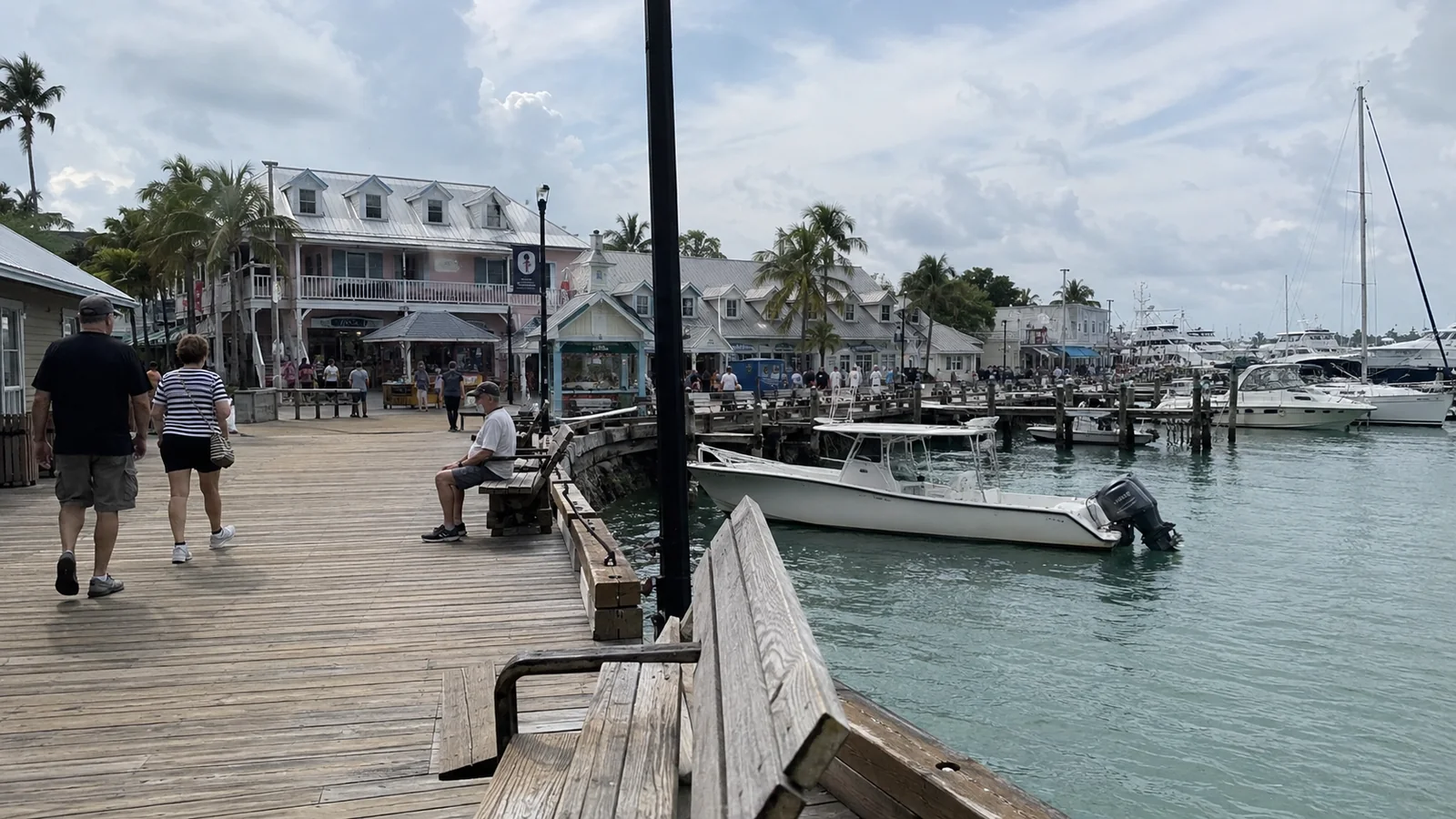 Visitors walking along a marina boardwalk lined with boats and waterfront buildings
