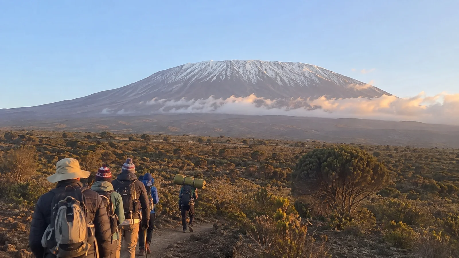 Hikers walking across a high plateau toward a snow-capped mountain