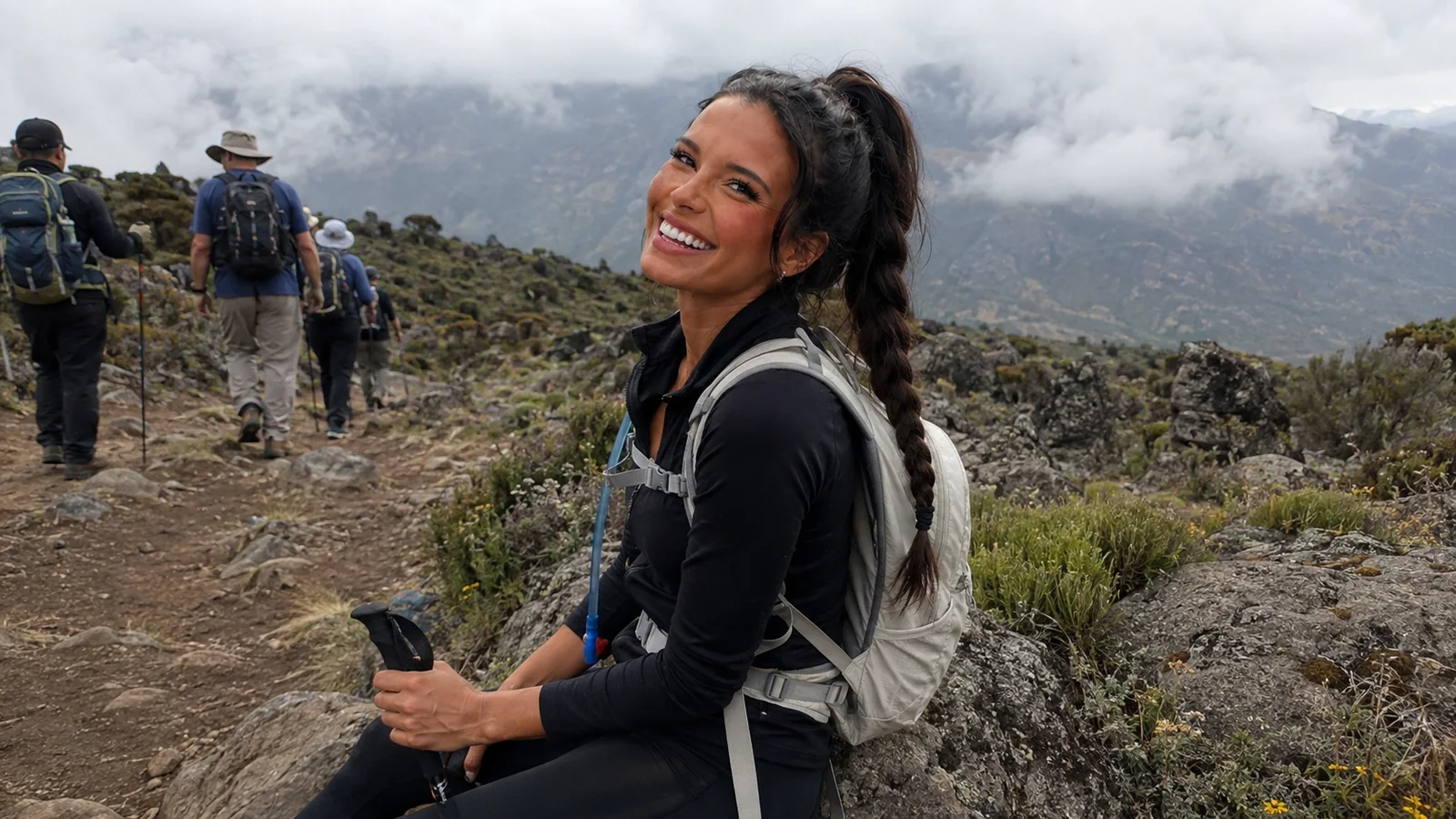 Smiling woman hiking on a rocky mountain trail with other hikers ahead