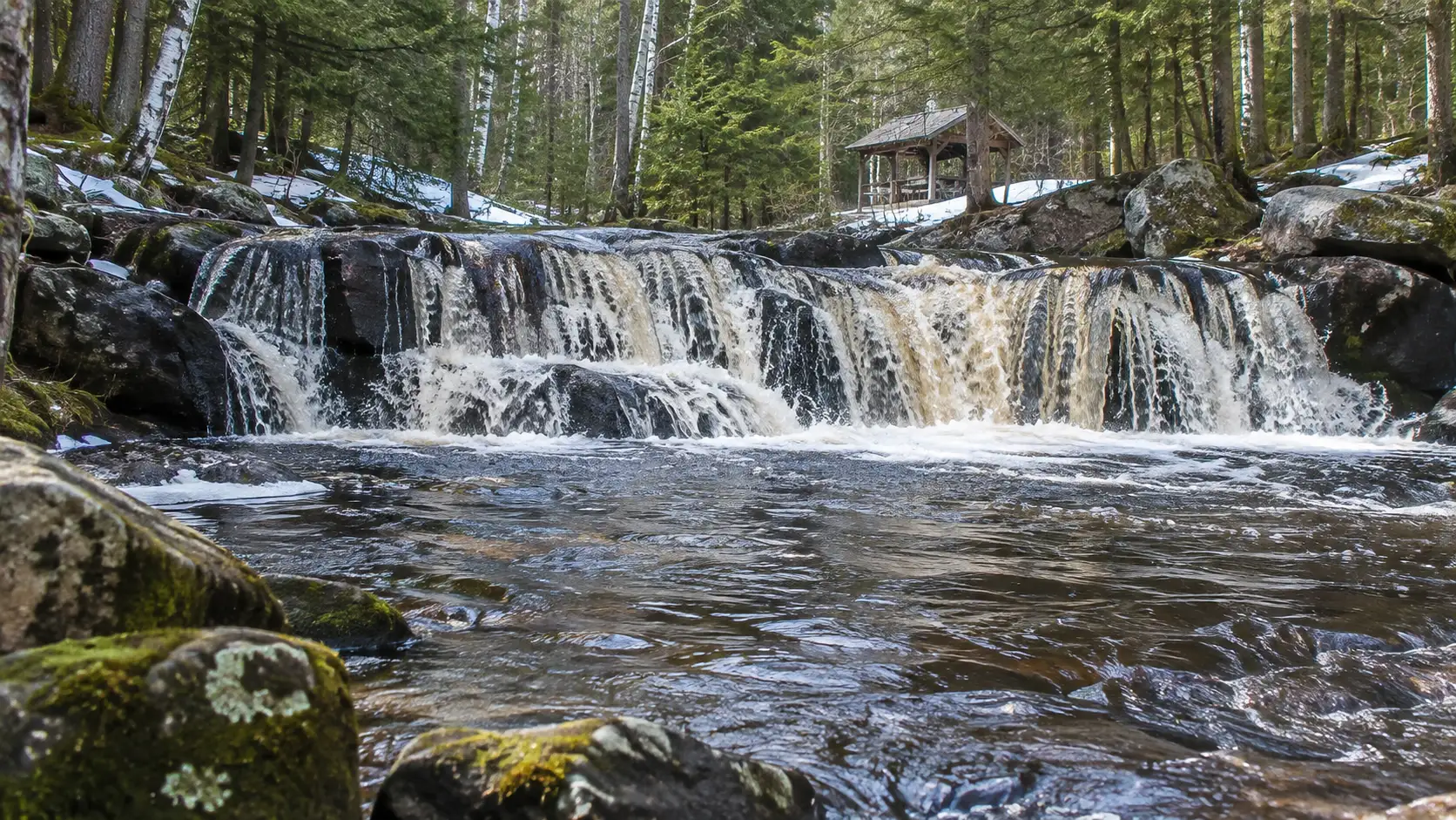 Kimball Falls spreading over a low rock ledge amid lingering snow and Northwoods pines in Wisconsin.