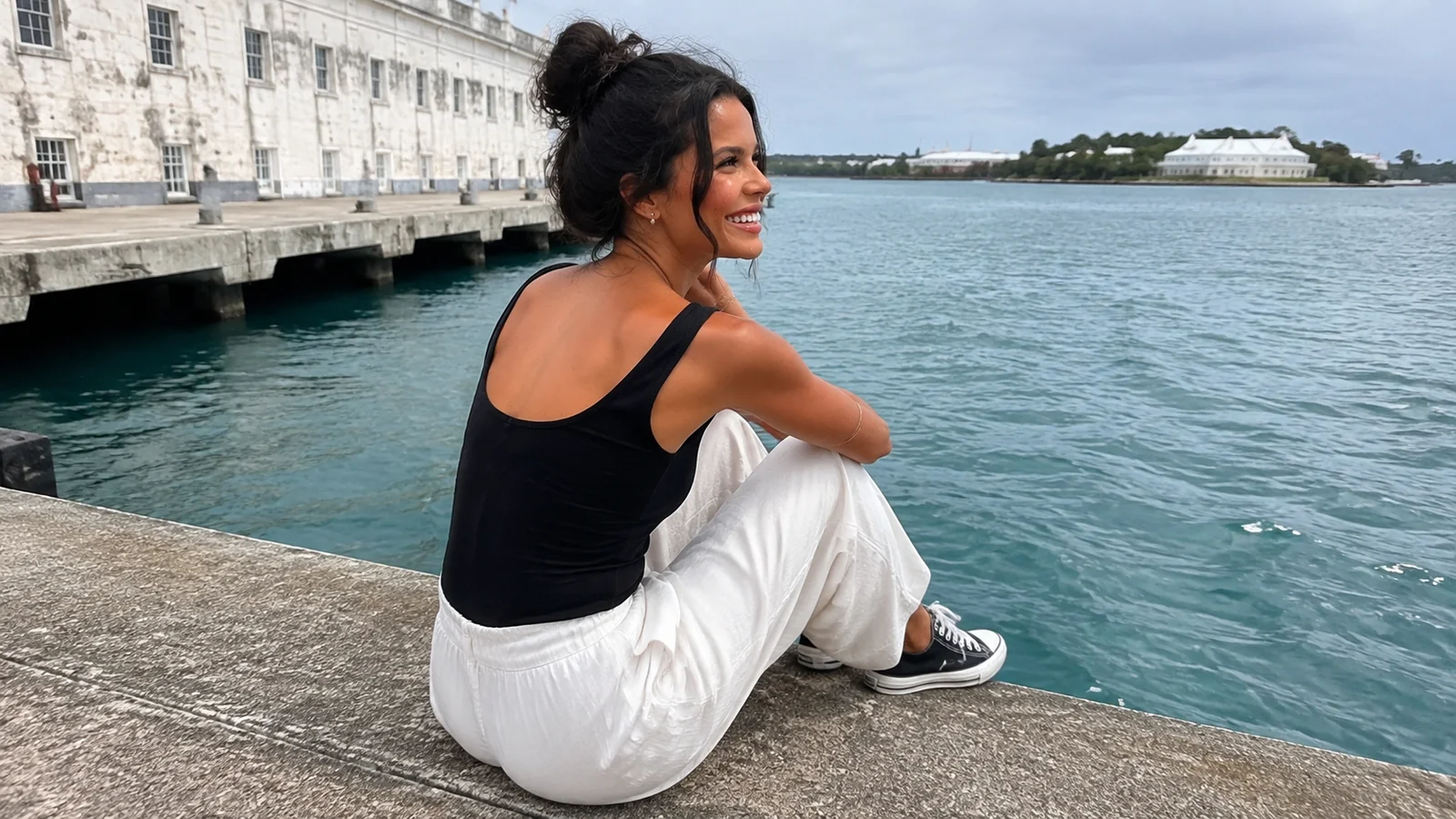 Woman seated on a stone wall beside turquoise harbor water