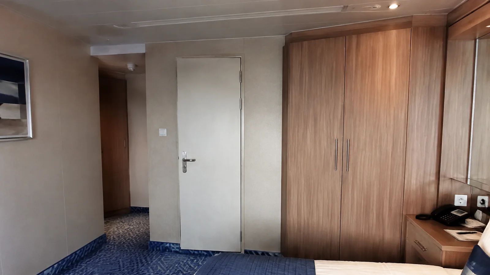 Closed pale door stands beside wood paneling and a stateroom desk.