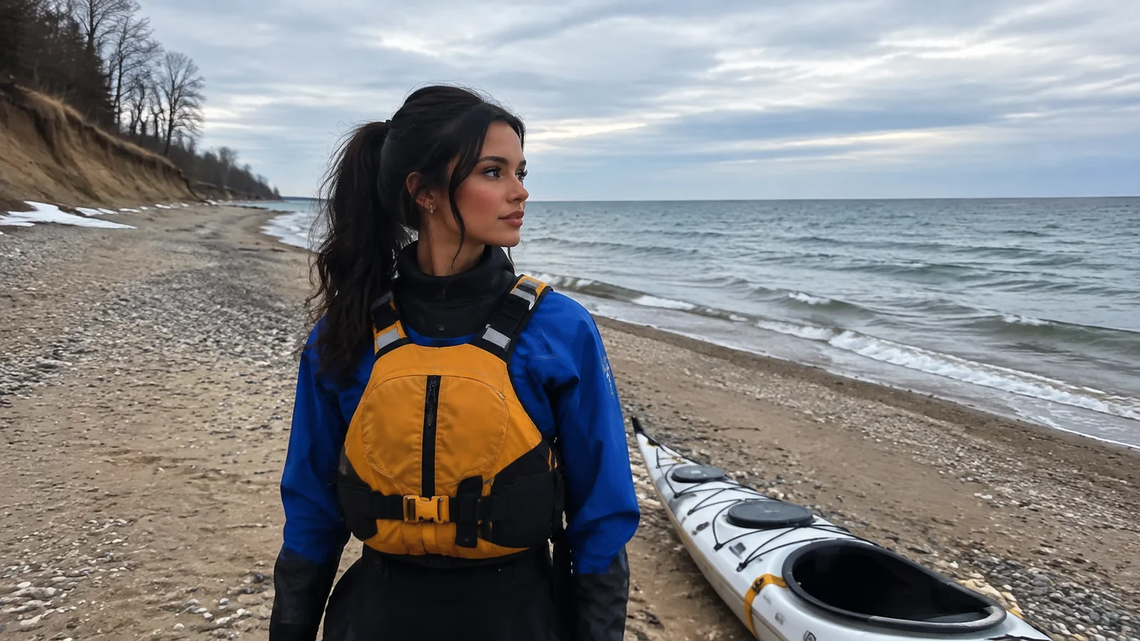 Woman wearing a life jacket stands beside kayaks on a beach.