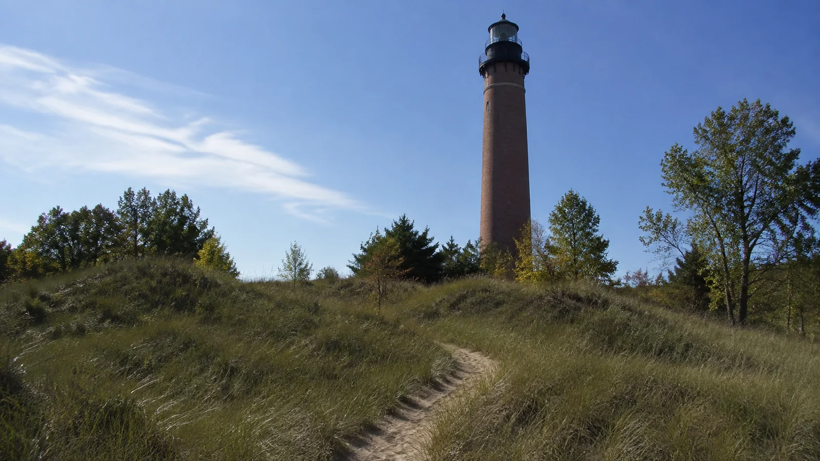 Tall brick lighthouse rises above grassy dunes and scattered trees.