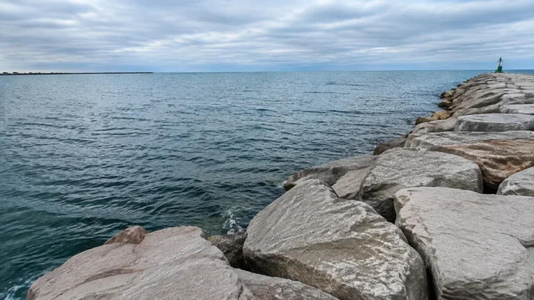 Rock breakwater extends into a broad lake beneath an overcast sky.