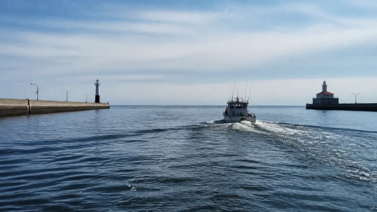 Fishing boat travels between harbor breakwaters topped by small lighthouses.