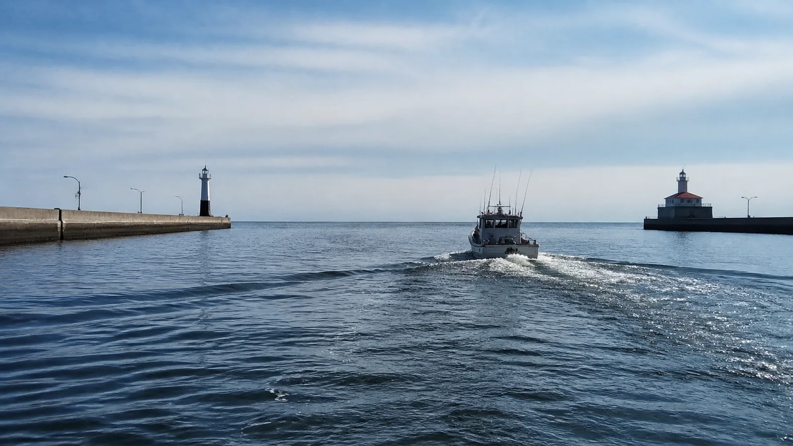 Fishing boat travels between harbor breakwaters topped by small lighthouses.
