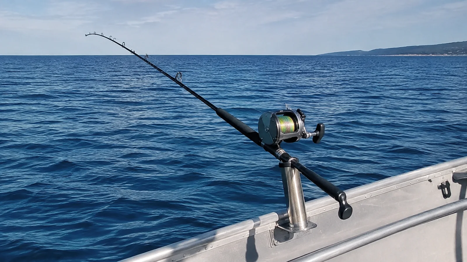 Fishing rod secured in a boat holder above blue lake water.