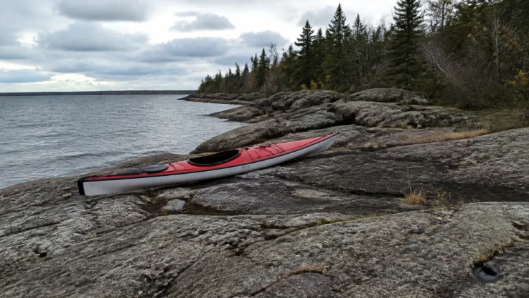 Red kayak rests on flat rocks beside a wooded lakeshore.