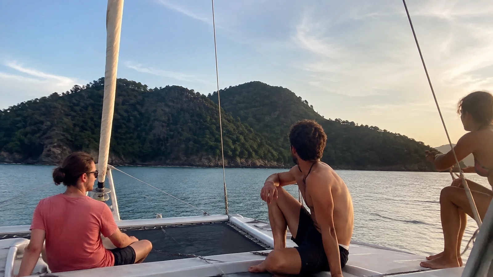 Passengers relaxing on a catamaran near green islands at sunset.