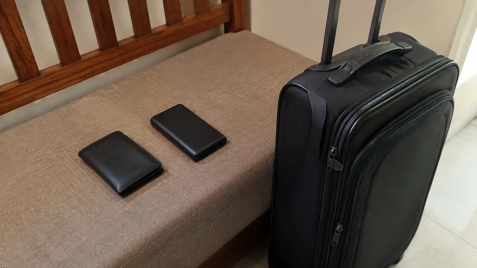 Black suitcase stands beside two small black cases on a bench.