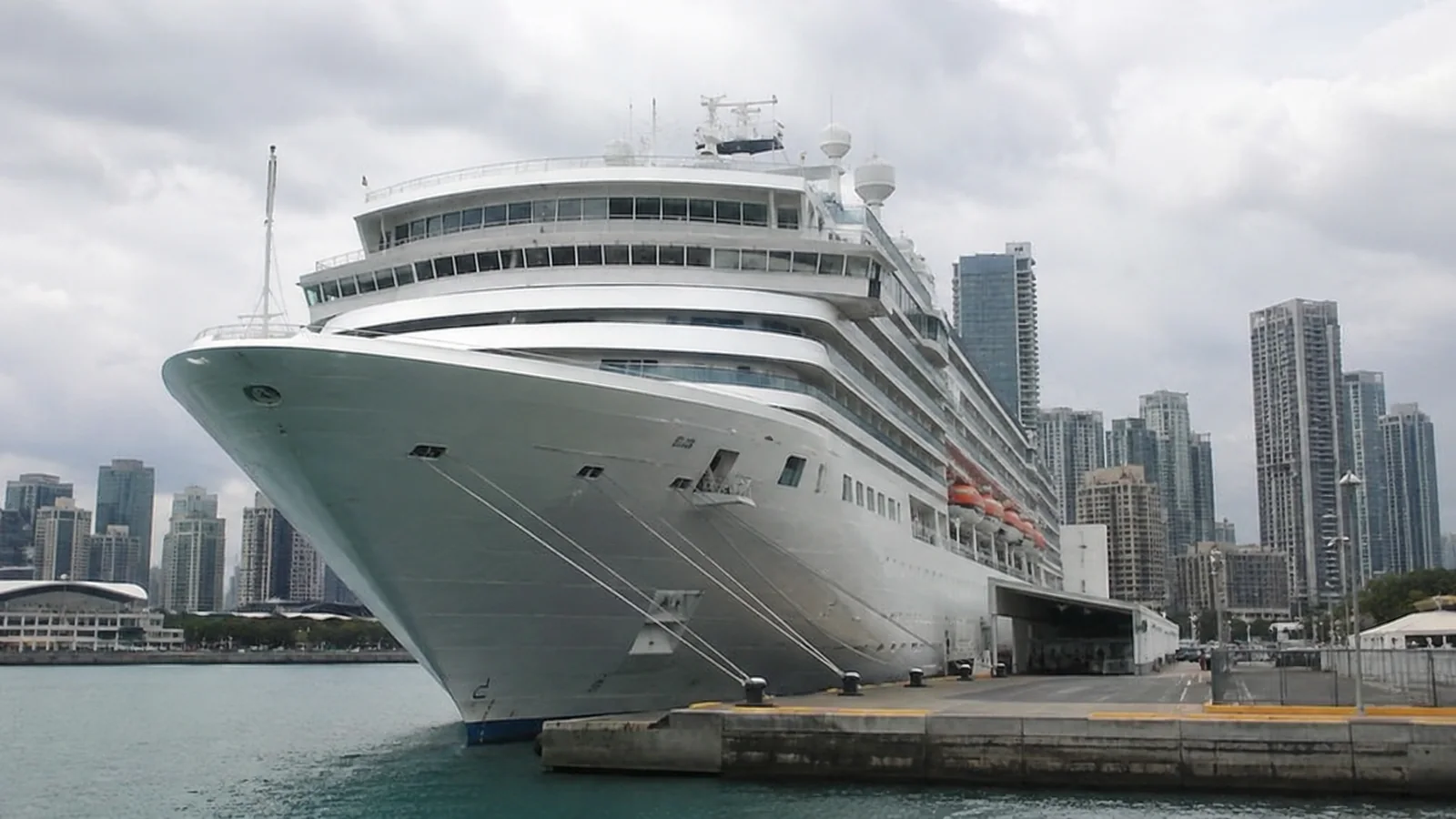 Large cruise ship is docked beside a waterfront city skyline.
