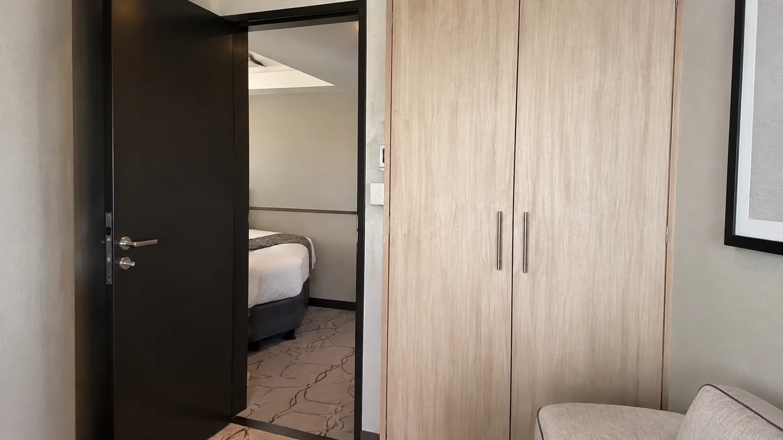 Wooden wardrobe stands beside an open doorway into an adjoining bedroom.