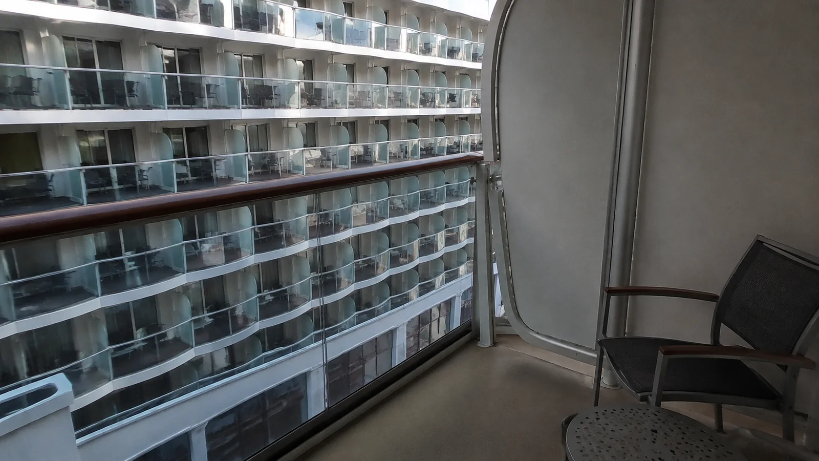 Balcony chair faces rows of stateroom balconies across a narrow open space.