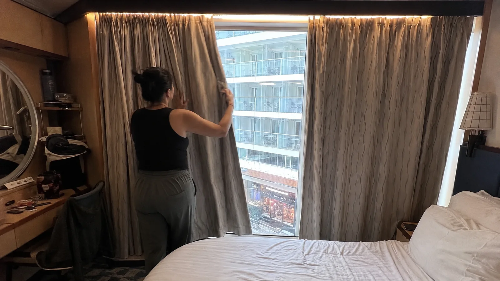 Passenger closing curtains over a window looking into the ship's promenade.