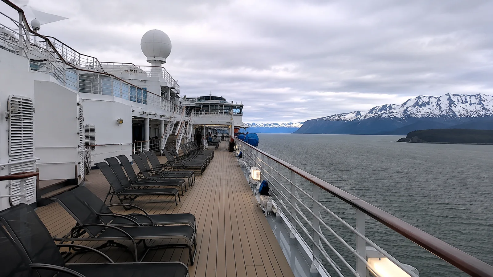 Empty outdoor cruise ship deck with lounge chairs and snowy mountains