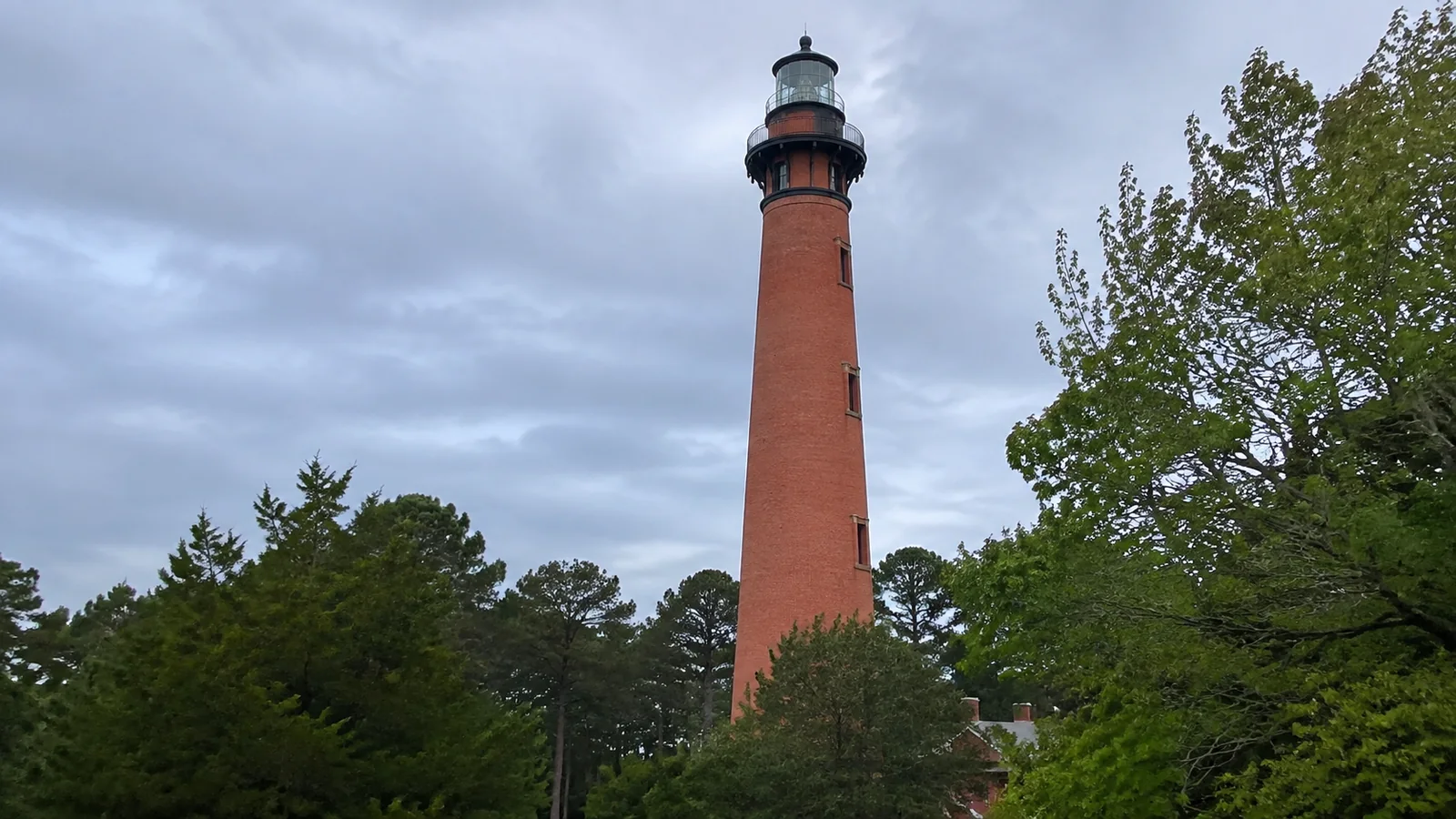 Tall red brick lighthouse rising above trees