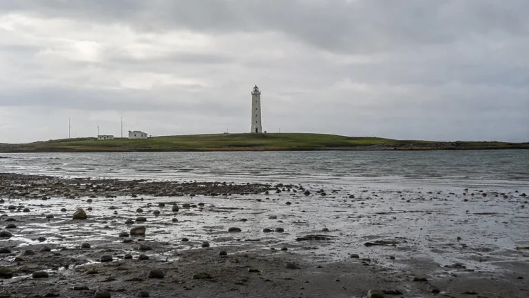 Slender white lighthouse beyond a rocky intertidal shoreline.