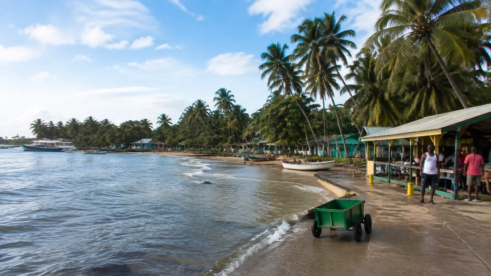 Palm-lined island waterfront with small cafes and a boat at the water's edge.
