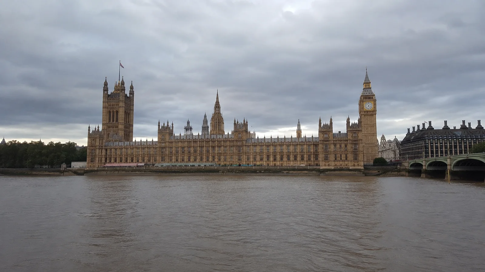Gothic riverside parliament building and clock tower beneath gray skies.