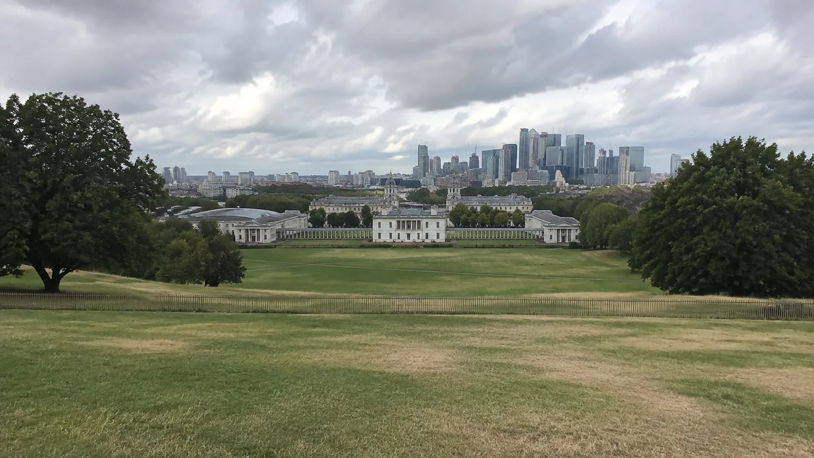 Broad grassy park slopes toward historic buildings and a distant skyline.