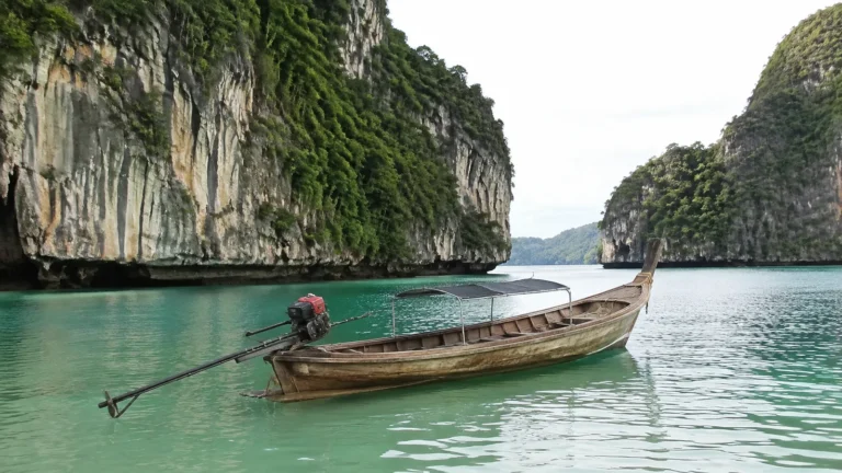 Wooden long-tail boat floats between steep limestone cliffs in green water.