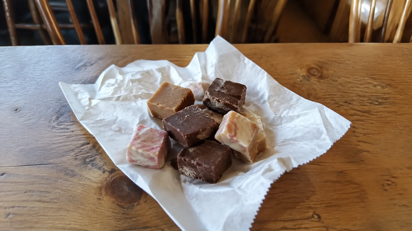Assorted pieces of fudge on paper atop a wooden table.