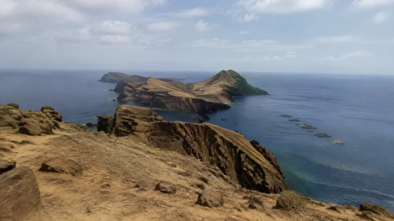 Rugged dry headland overlooks rocky islands in deep blue water.