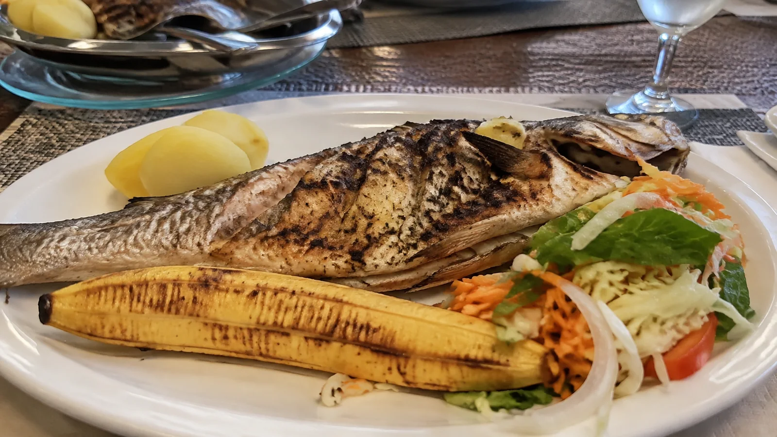 Grilled whole fish with potatoes, vegetables, and plantain on a plate.