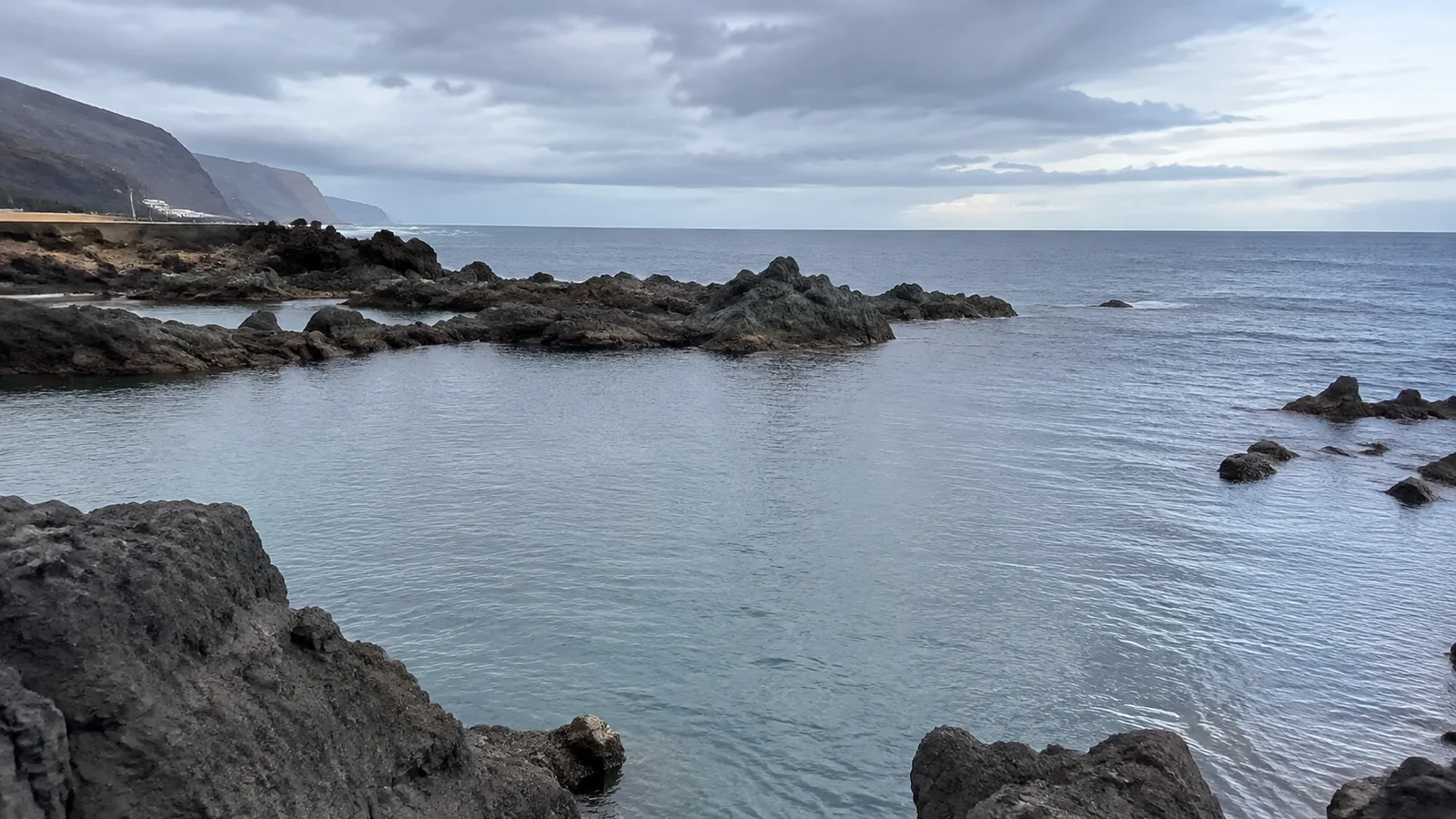 Rocky natural coastal pools beside calm gray ocean water.