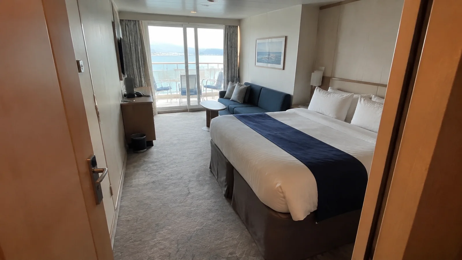 Bright balcony cabin with a double bed and blue sofa.