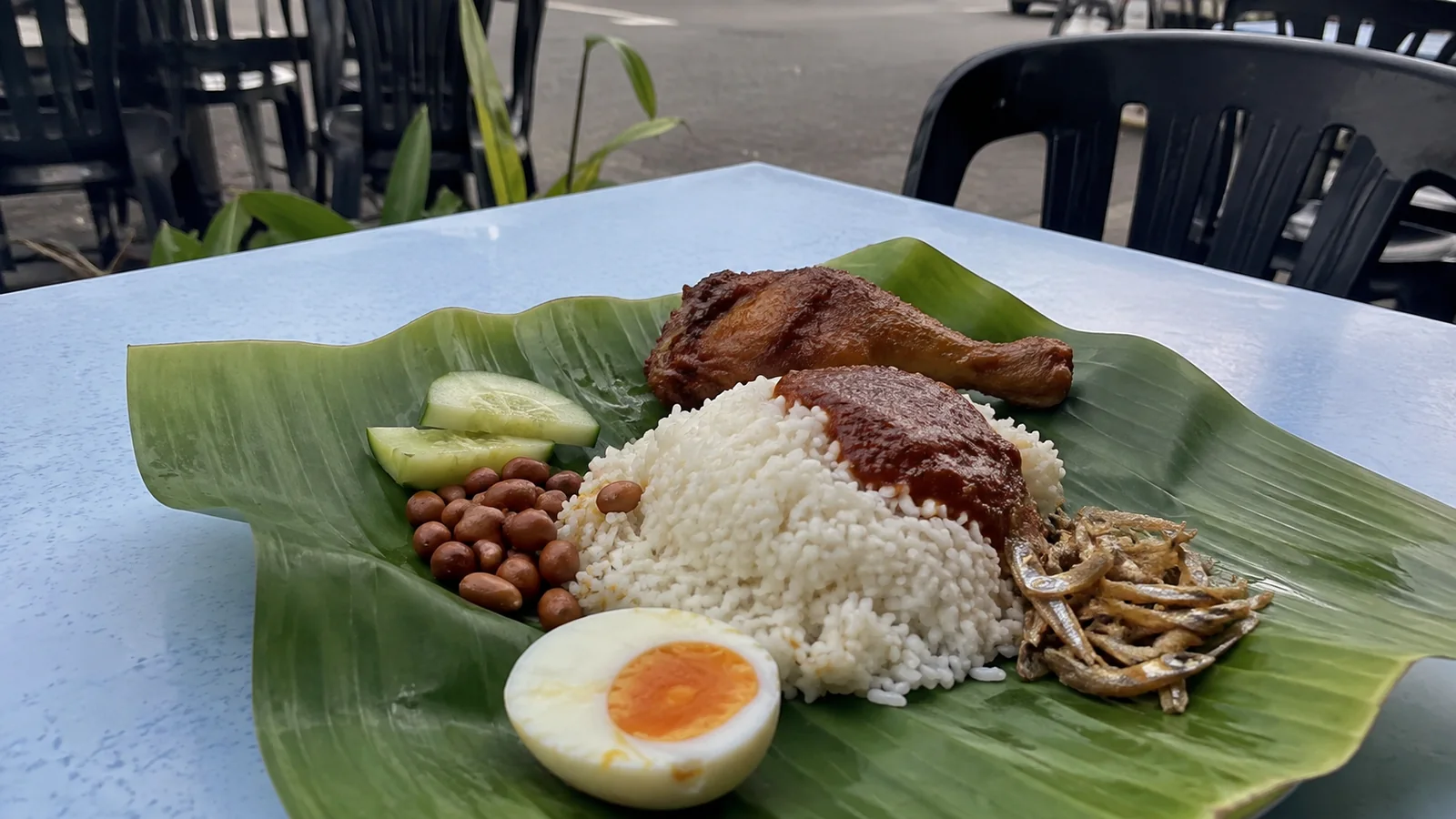 Rice, chicken, egg, cucumber, and peanuts served on a banana leaf.