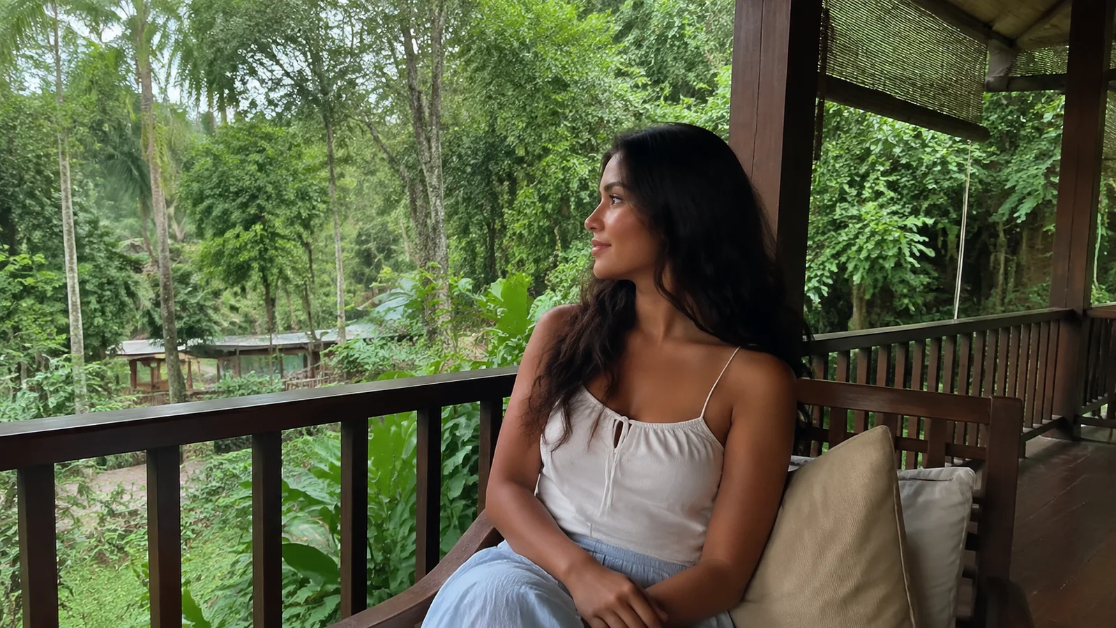 Woman rests on a shaded wooden veranda overlooking tropical greenery.