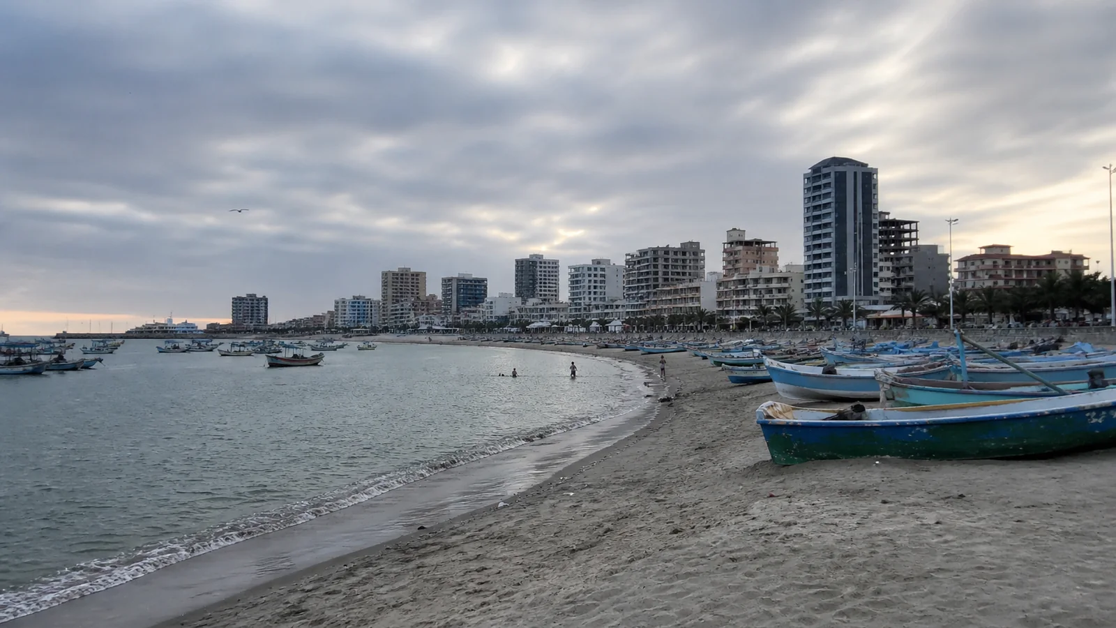 Small fishing boats pulled onto a beach beside a city skyline.
