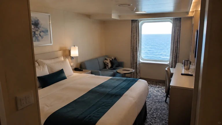 Compact stateroom contains a double bed, sofa and ocean window.
