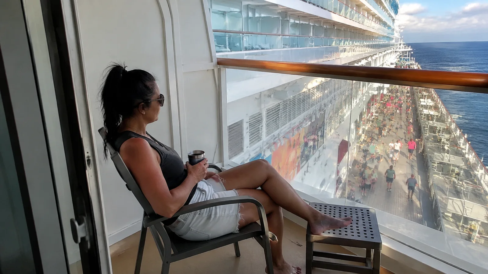 Woman sits on a balcony overlooking a busy ship promenade.