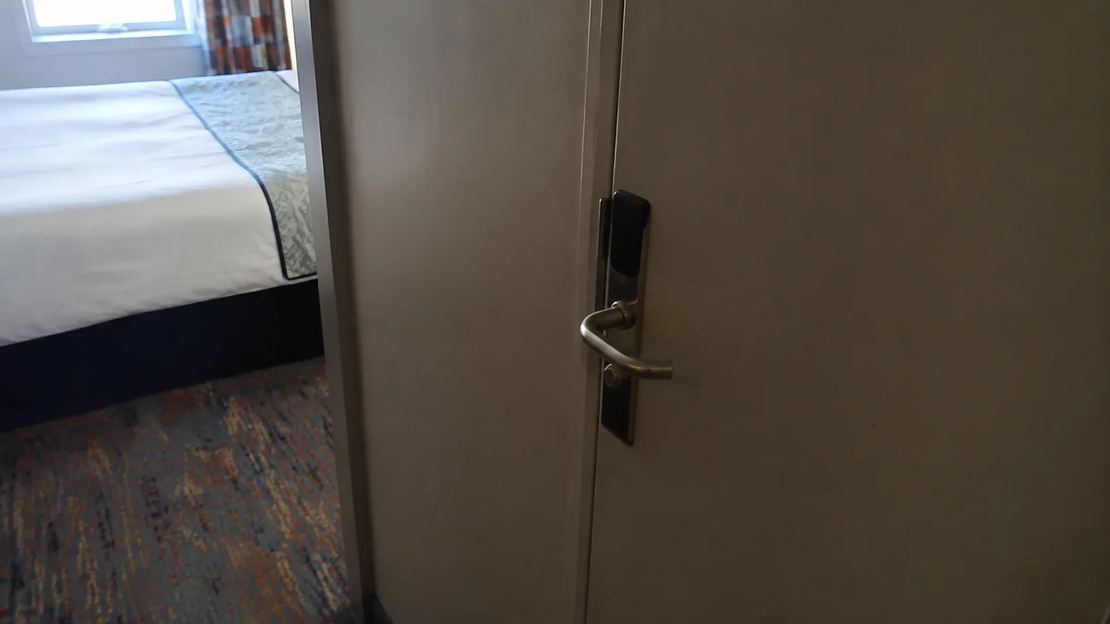 Close view of a stateroom door handle beside a bed.