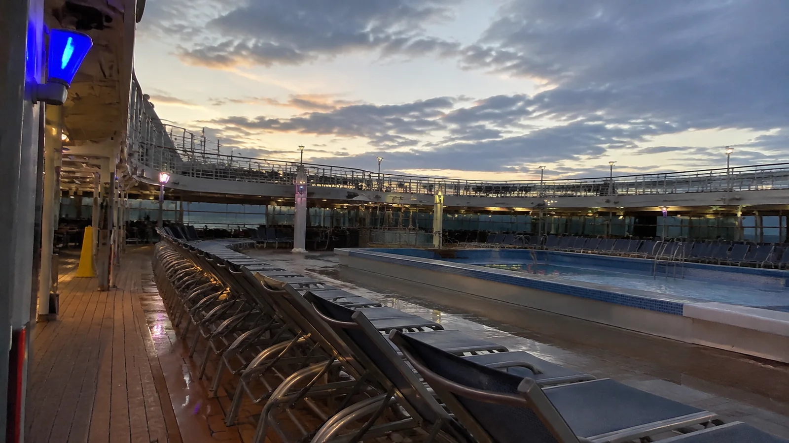 Rows of empty loungers line a ship pool at dusk.