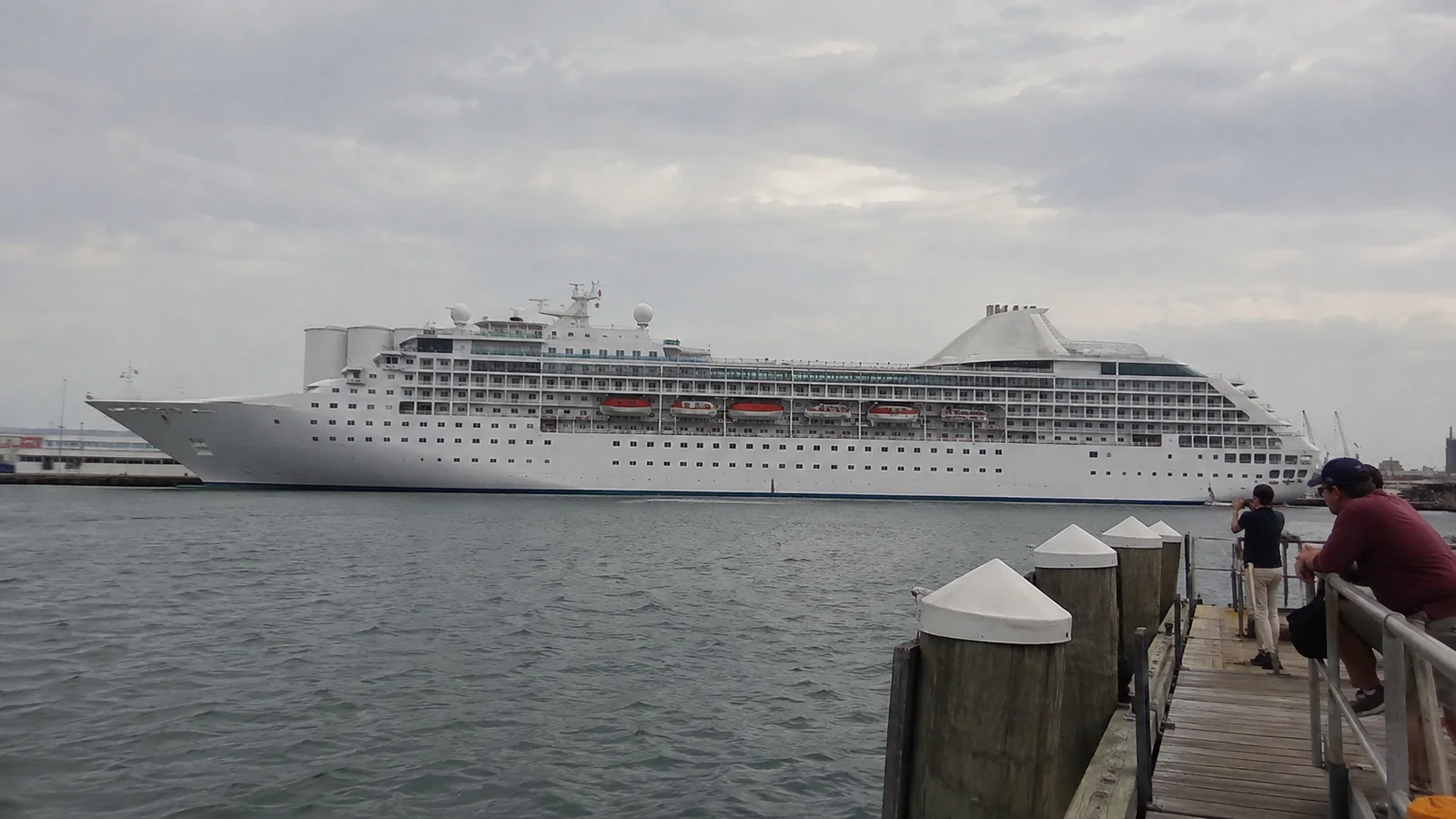 Cruise ship across the harbor from a wooden pier.