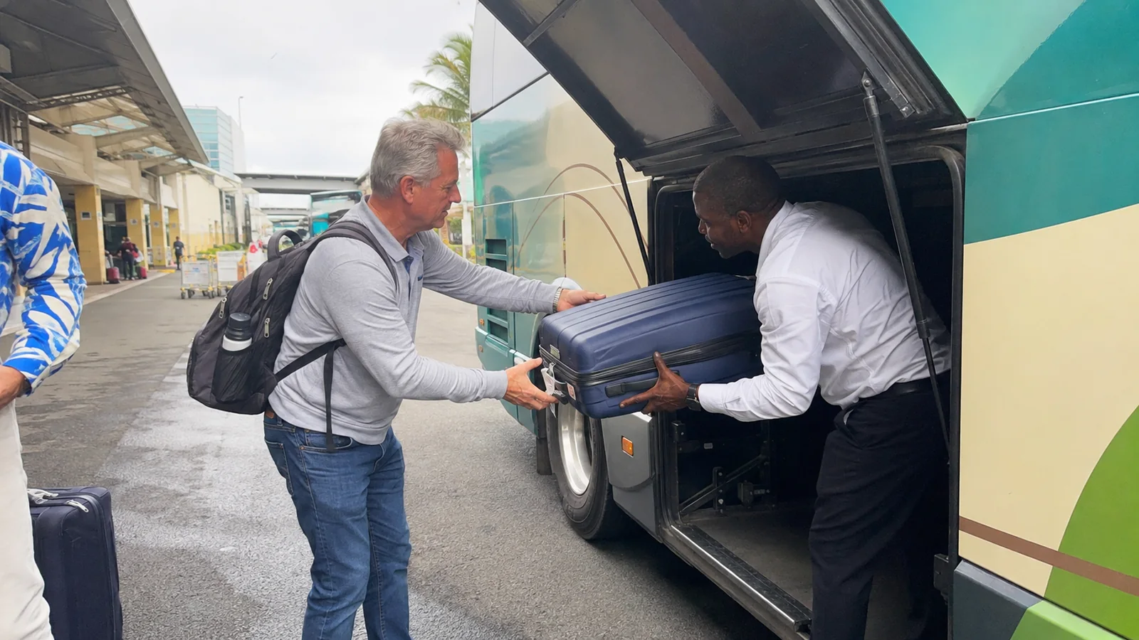 Traveler handing a suitcase to a driver at a coach luggage compartment.