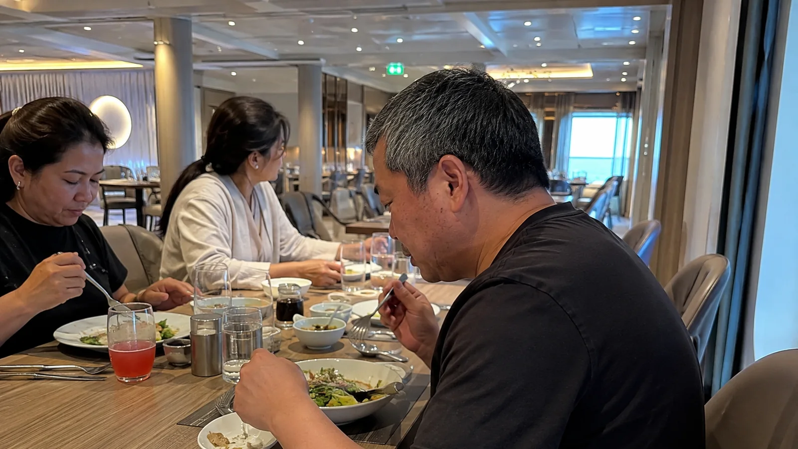 Passengers eating together in a bright ship dining room.