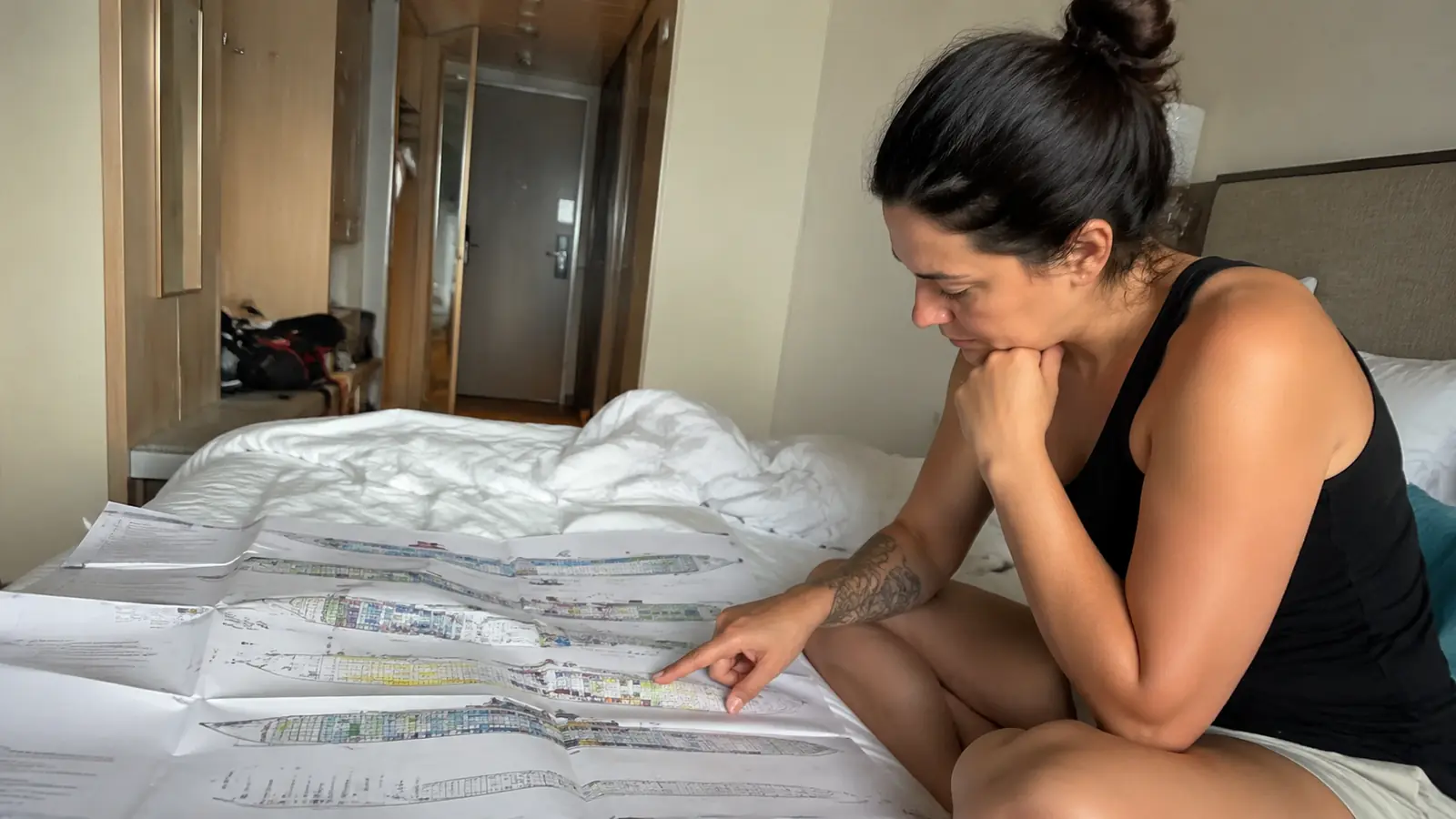 Woman sitting on a cruise cabin bed reviewing large printed deck plans